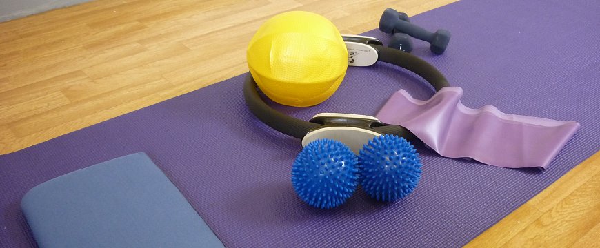 Pilates mat with small pilates equipment on it such as toning circle, overball, spikey balls.