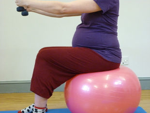 Pregnant woman sitting on a pink stability ball holding weights