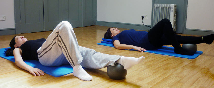 Two Women lying on mats doing a Post Natal Pilates class