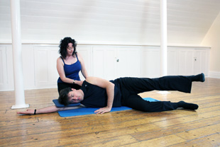Pilates Teacher assisting client doing a Pilates matwork exercise